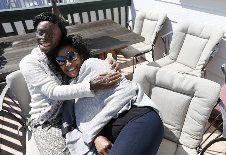 Atsede Niguse hugs Menbere Aklilu as they sit on a deck.