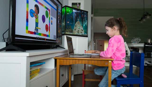A child in front of  a laptop and large screen.