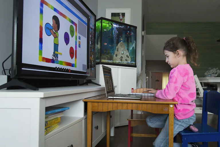 A child in front of a laptop and large screen.