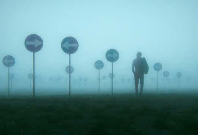 A man in a heavy mist surround by signs pointing in opposite directions. 