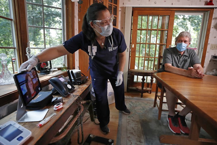 A nurse setting up a telehealth appointment for an older man in his home.