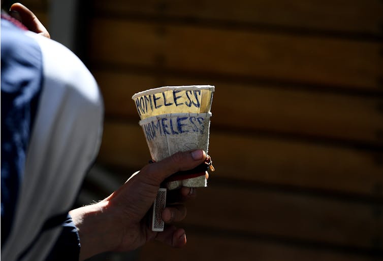 Man holds out begging cup with the word homeless on it