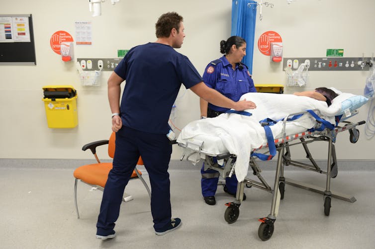 Ambulance and medical staff attend to a patient in a hospital emergency department