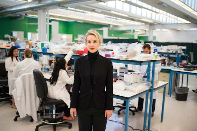 A woman dressed in black stands in a lab and looks at the camera