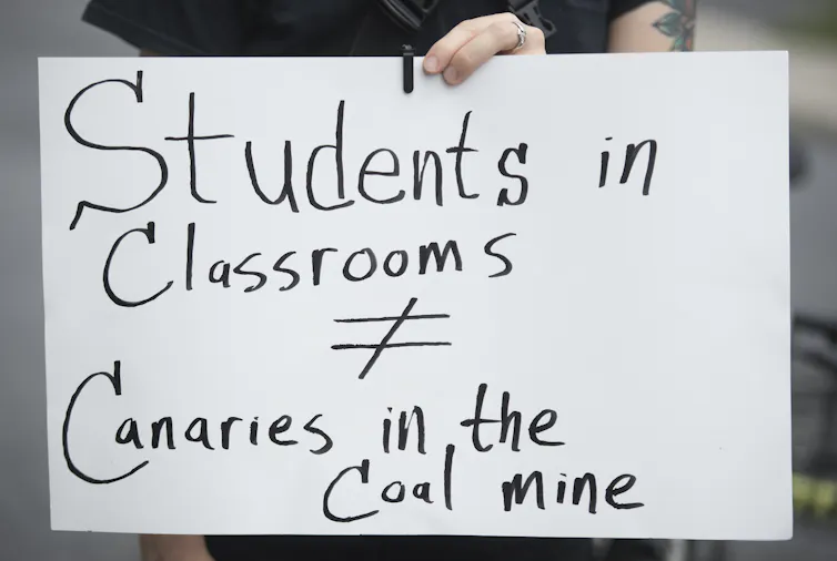 A protester holds up a sign that says Students in Classrooms do not equal Canaries in the Coal Mine