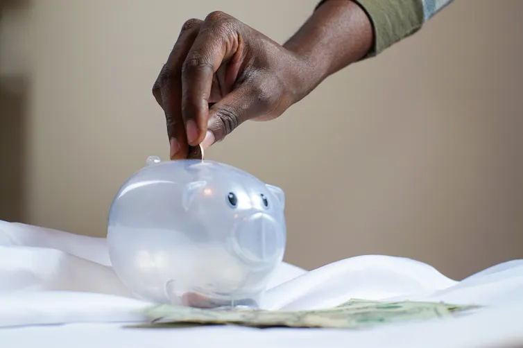 A hand drops coins into a piggy bank.
