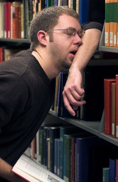Weary man leaning against shelf of books