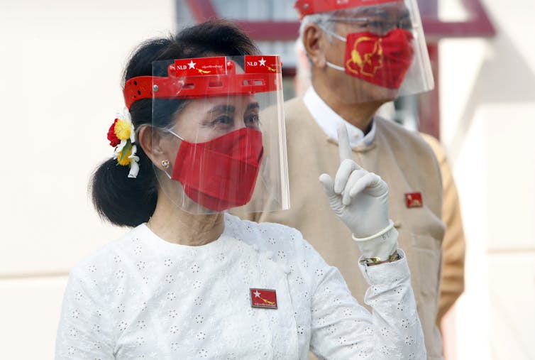 Myanmar leader Aung San Suu Kyi gestures while wearing a face shield, mask and glove.