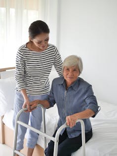 A woman helping her mother stand up with the use of a walker.