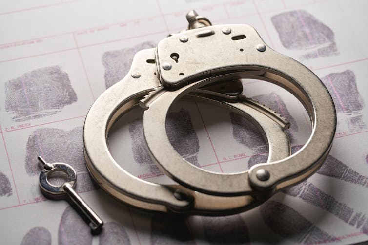 A pair of handcuffs lies on top of a fingerprint card.