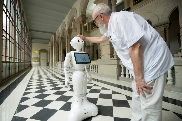 A man in white medical uniform pats the head of a white robot.