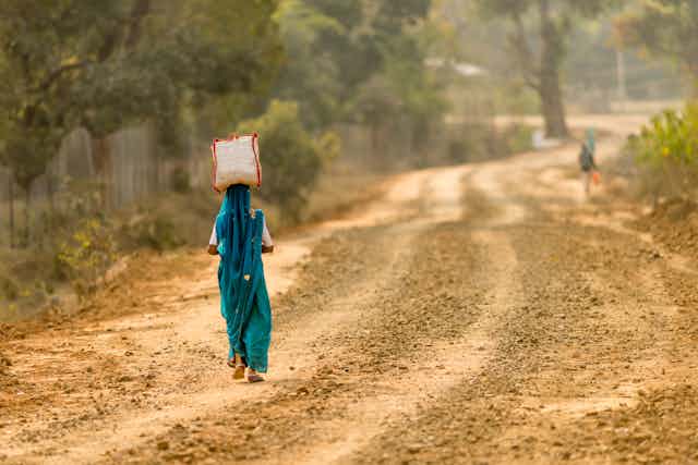 A woman in Indian dress walks down a dirt road.