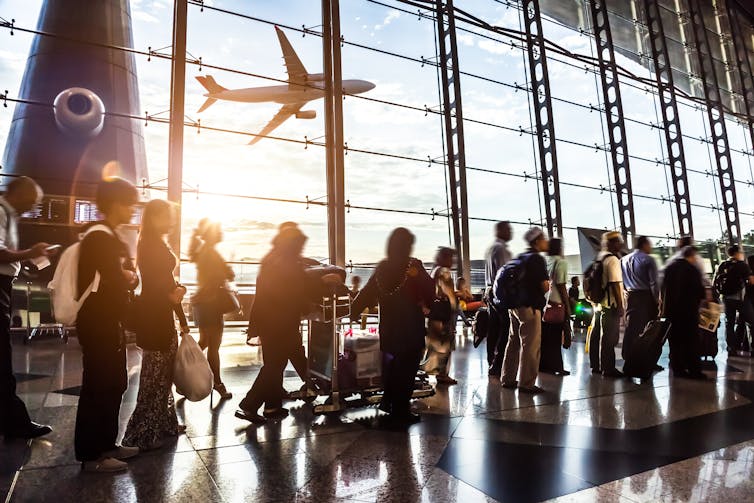 Line of people waiting with aeroplane visible in window behind