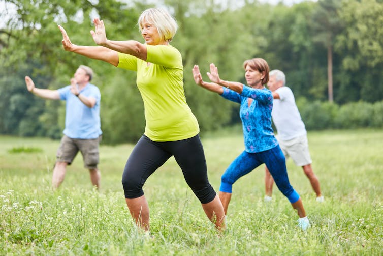 Four older adults performing tai chi outdoors.