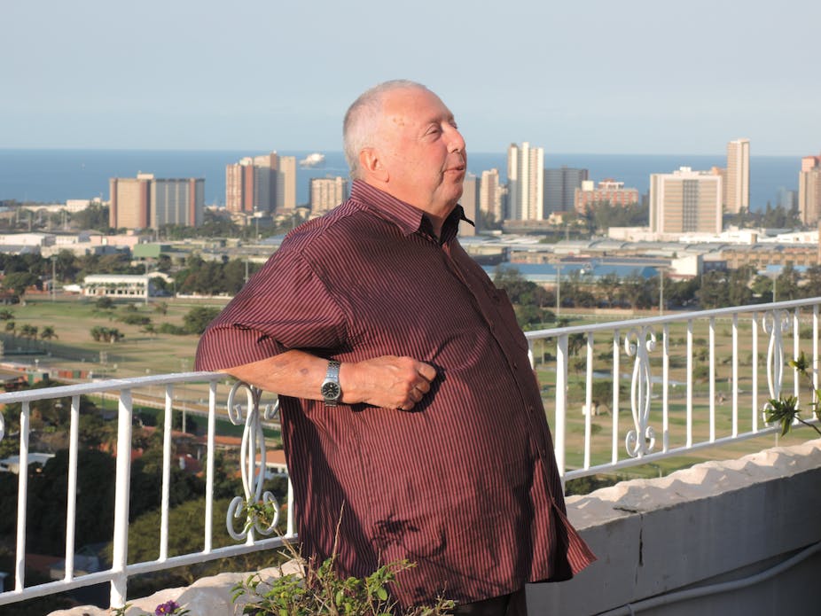 Man standing near a balcony with a view of the city and ocean behind him.