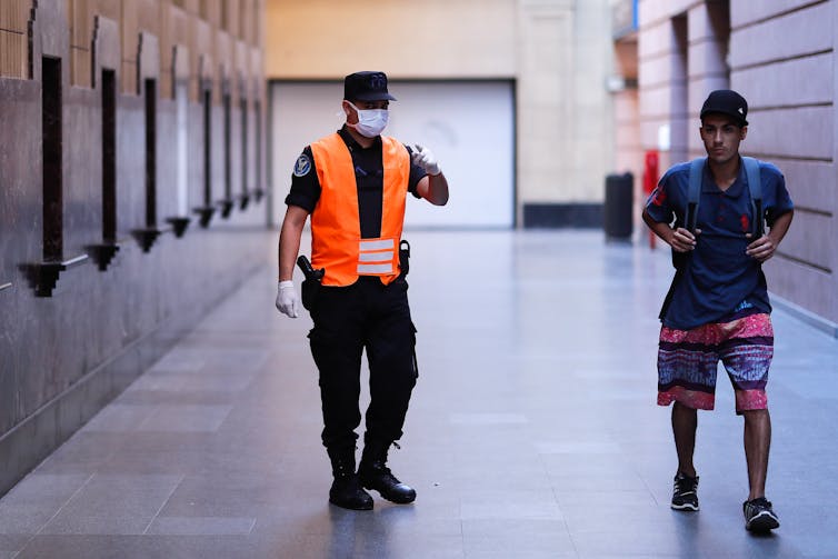 Official wearing hi-viz jacket and mask points at young man on the street.