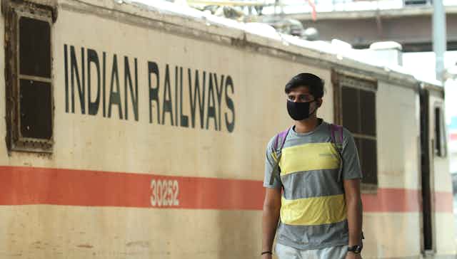 Un hombre con mascarilla negra en un andén ante un vagón con el texto Indian Railways.
