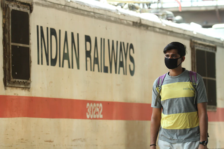 Un hombre con mascarilla negra en un andén ante un vagón con el texto Indian Railways.