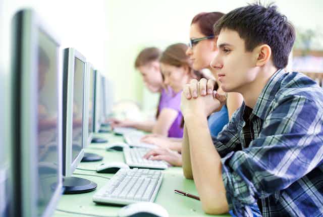 Cinco estudiantes sentados en línea delante de sendos ordenadores.