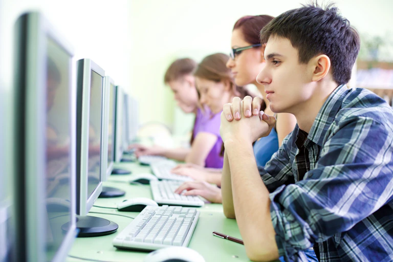 Cinco estudiantes sentados en línea delante de sendos ordenadores.