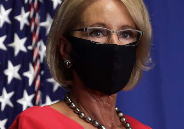 Education Sec. Betsy DeVos, wearing a face mask near an American flag