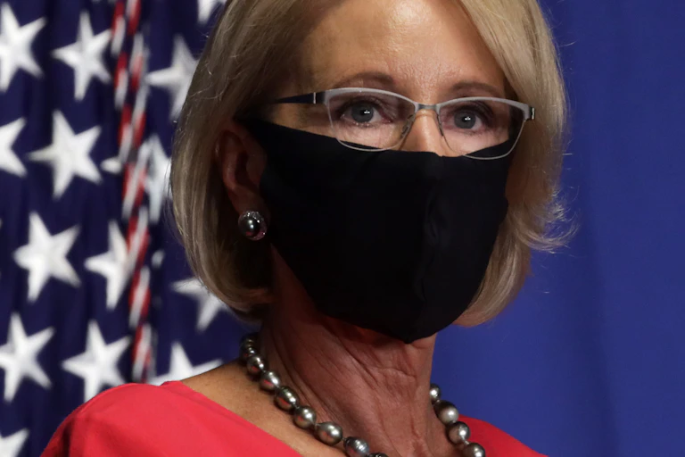 Education Sec. Betsy DeVos, wearing a face mask near an American flag