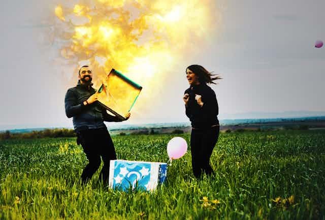 With his excited wife looking on, a man opens a box as a flame shoots out of it.