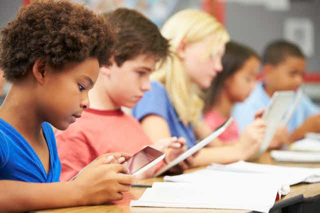 A row of schoolchildren working on tablets at their desks