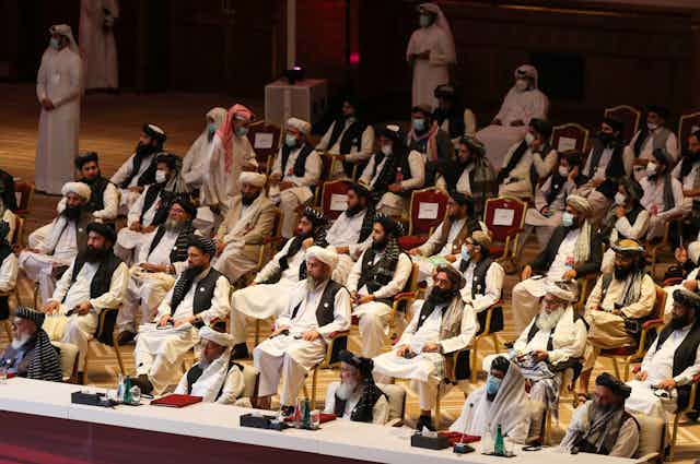 Dozens of Taliban members sit in an auditorium-style setting