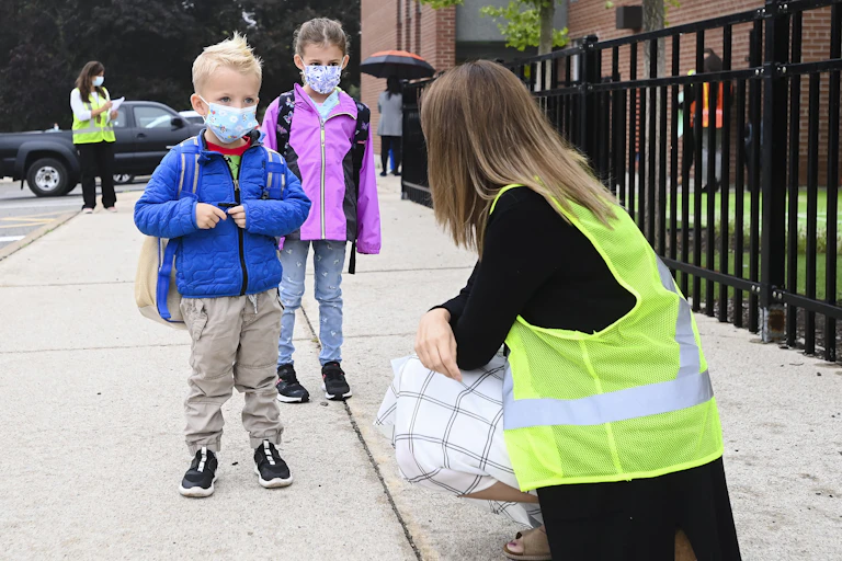 Two children speak to a teacher who is crouched.