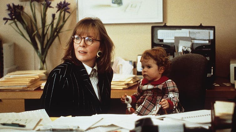 Movie still. Diane Keaton and a baby at a desk.