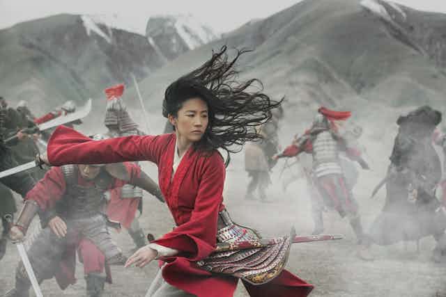 Mulan, in red, holds a sword in battle