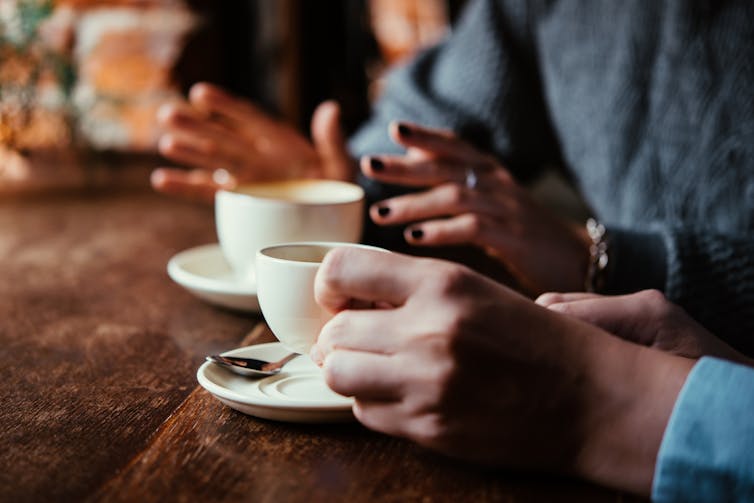 Two women in a cafe talking and having coffee. Image focuses on their cups and hands.