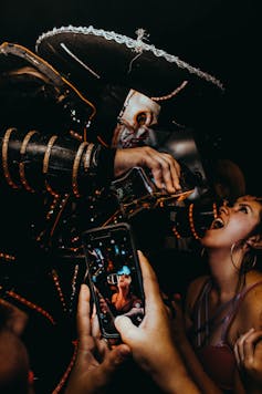 A smartphone in the foreground filming as a man in a costume pours liquor into a young woman's mouth