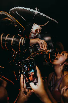 A smartphone in the foreground filming as a man in a costume pours liquor into a young woman's mouth