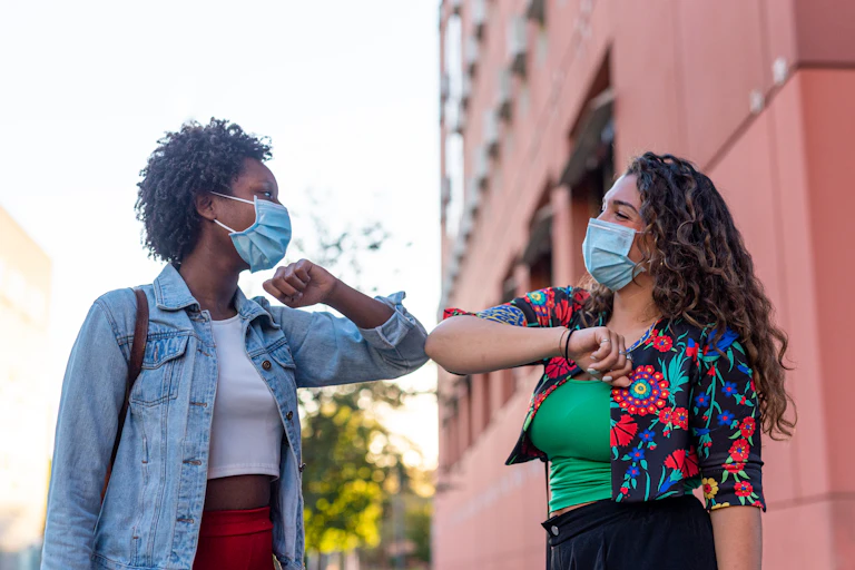 Two women wearing masks elbow bumping