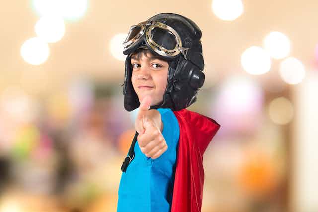 Boy wearing a superhero costume and aviator glasses doing a thumbs up
