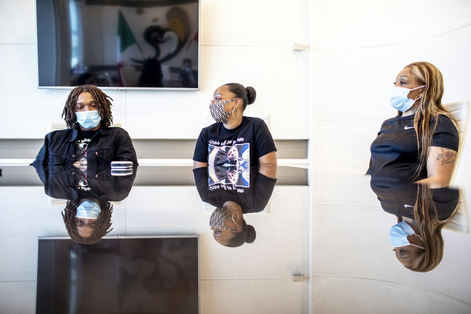 Three people wearing masks are seen sitting at a conference table.