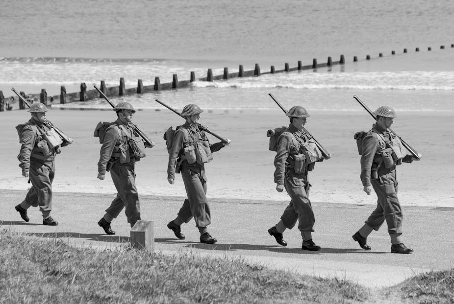 WWII soldiers marching single file on beach