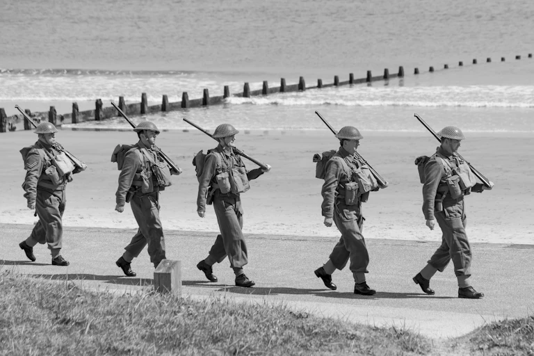 WWII soldiers marching single file on beach