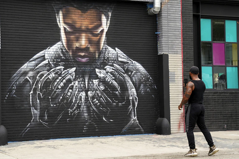 A man photographs a mural on the street.