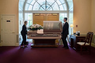 Two people position a casket in a funeral home