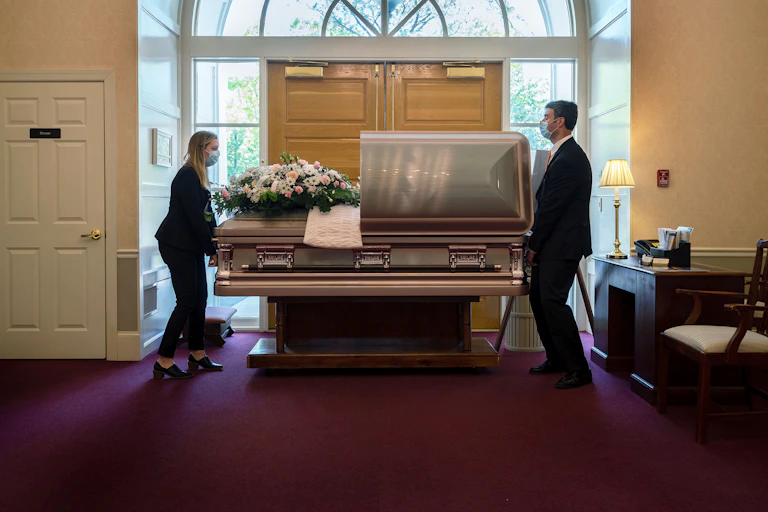 Two people position a casket in a funeral home
