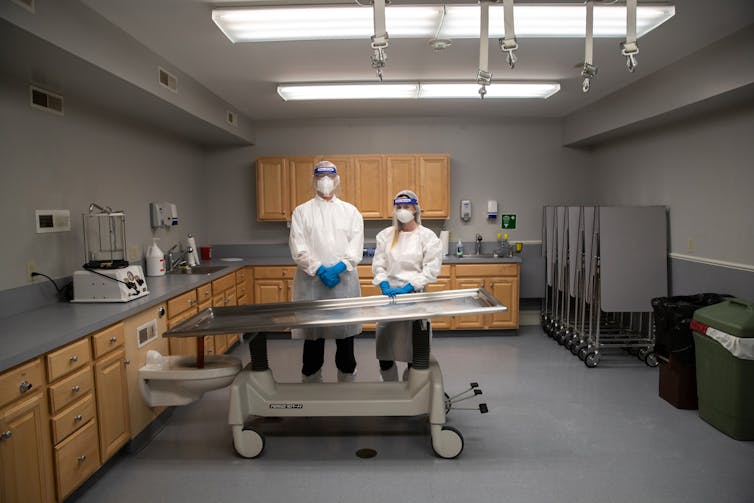 Two funeral home staff stand behind a mortuary table