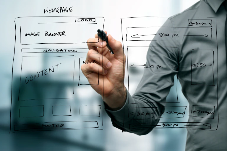 A man's hand writing on a glass board to show the basics of a webpage design.
