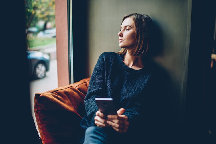 Woman holding phone, looking out a window.