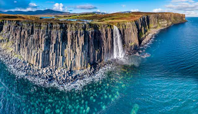 The sheer coastline of the Isle of Skye with blue, shallow coastal water.