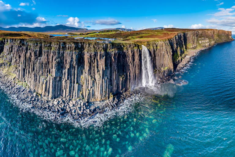 The sheer coastline of the Isle of Skye with blue, shallow coastal water.
