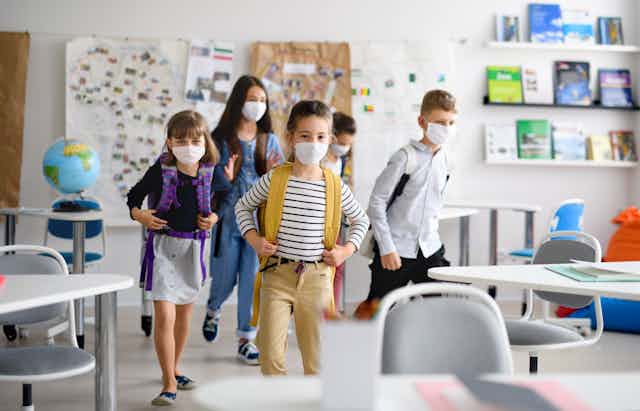 Cinco niños y niñas con mochila y mascarillas entran en un aula.