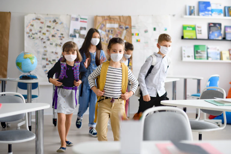 Cinco niños y niñas con mochila y mascarillas entran en un aula.